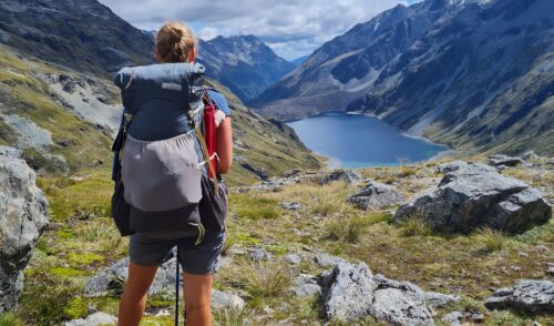 Julia Rebuck steht mit Rucksack in einer Seen - Berglandschaft in Neuseeland